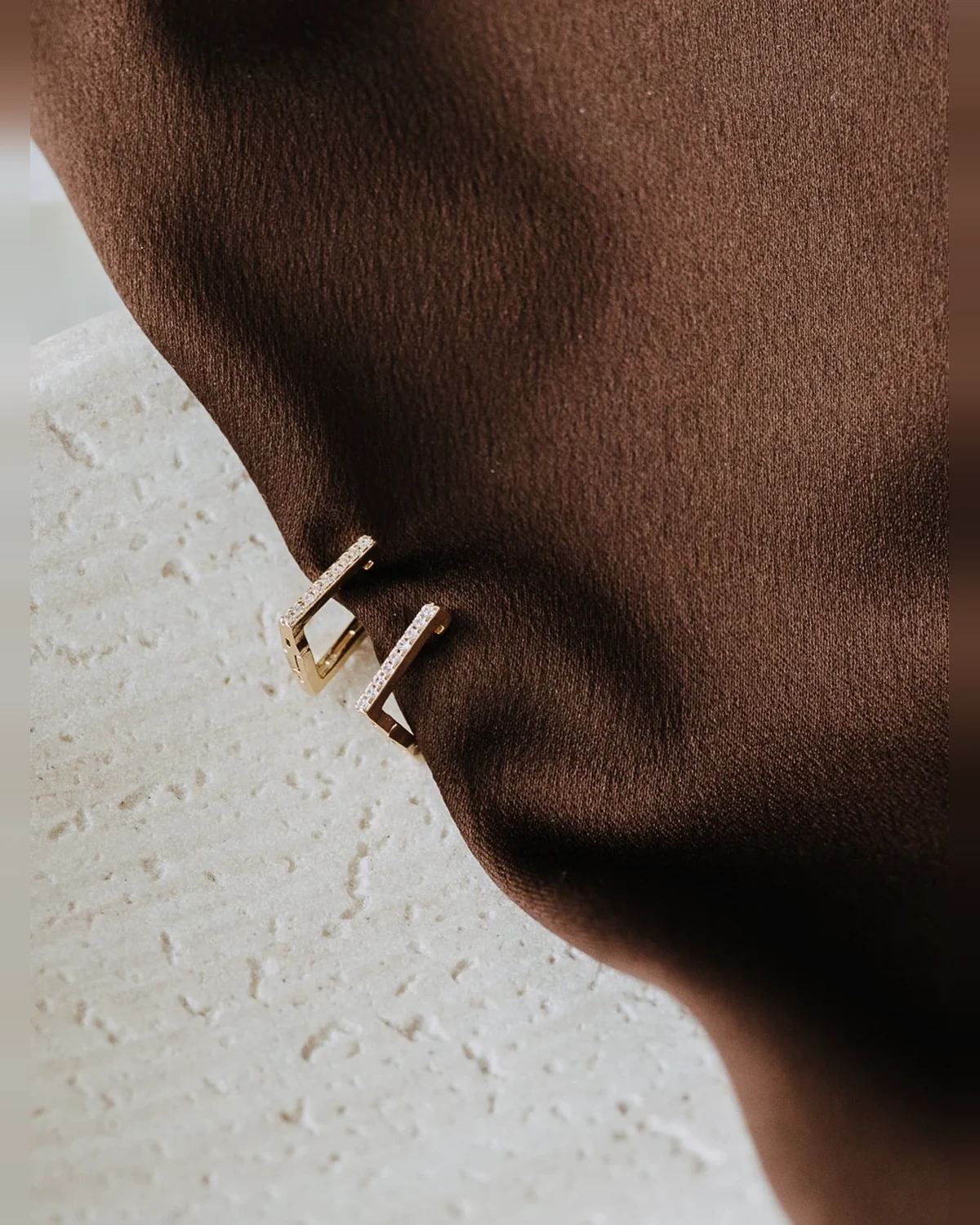 Luna Hoops by Sydney Rose Co., gold rectangular pavé hoops resting on brown satin and a travertine tray