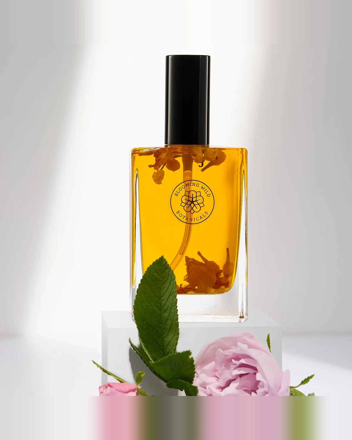 Blooming Wild Botanicals Queen of Hearts body oil in a clear bottle with rose petals